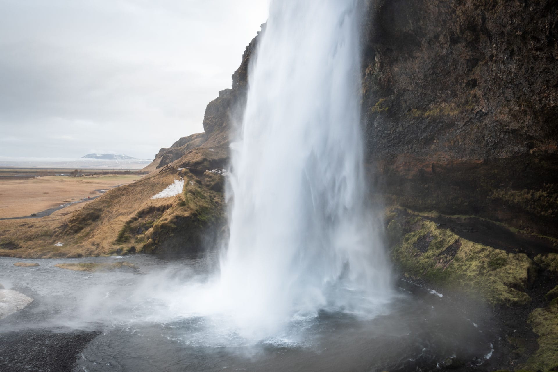 View from the hollow behind Seljalandsfoss onto the falling column of water, the wide coastal plain beyond